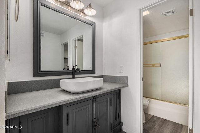 full bathroom featuring shower / bath combination with glass door, toilet, vanity, and hardwood / wood-style flooring