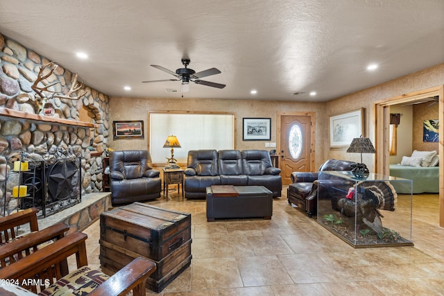 living room featuring a textured ceiling, ceiling fan, and a stone fireplace