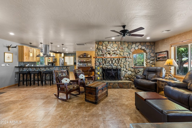 living room with a wealth of natural light, ceiling fan, a textured ceiling, and a fireplace