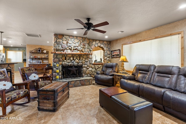 living room featuring ceiling fan, a textured ceiling, and a stone fireplace