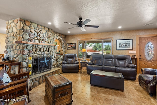 tiled living room with a textured ceiling, ceiling fan, and a stone fireplace