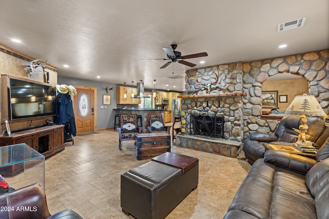 living room with a textured ceiling, ceiling fan, and a fireplace