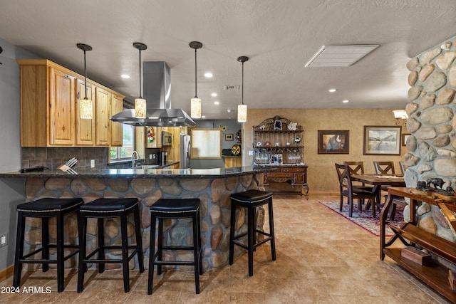 kitchen featuring stainless steel refrigerator, tasteful backsplash, a kitchen bar, kitchen peninsula, and wall chimney exhaust hood