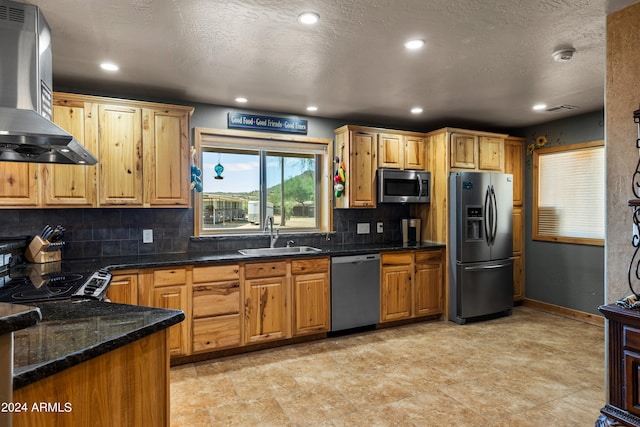 kitchen featuring appliances with stainless steel finishes, sink, decorative backsplash, wall chimney range hood, and dark stone counters