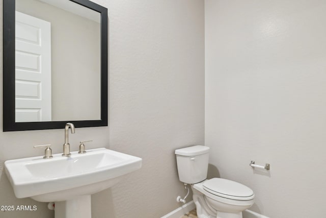 half bath with toilet, baseboards, and a sink