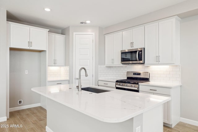 kitchen featuring wood tiled floor, a kitchen island with sink, appliances with stainless steel finishes, and a sink