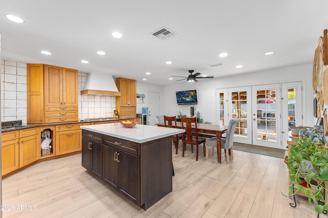 kitchen featuring decorative backsplash, custom exhaust hood, french doors, light wood finished floors, and stainless steel gas stovetop