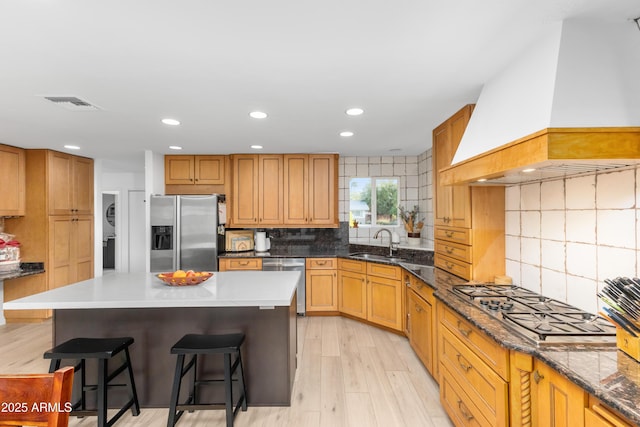 kitchen featuring visible vents, custom exhaust hood, a kitchen bar, a sink, and stainless steel appliances