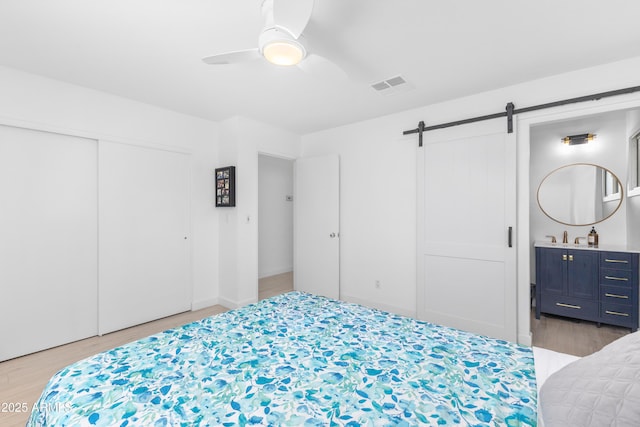 bedroom with a closet, light wood-type flooring, a barn door, and visible vents