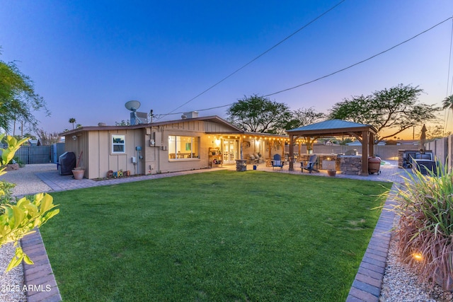 back of property at dusk featuring board and batten siding, a lawn, a patio area, a gazebo, and a fenced backyard