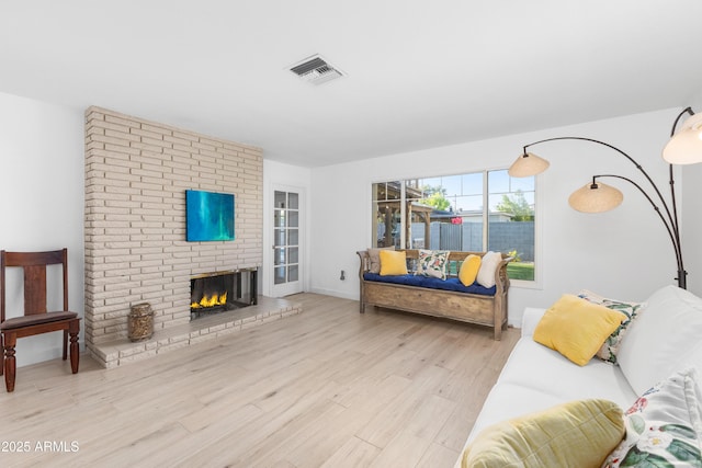 living area featuring a brick fireplace, wood finished floors, and visible vents