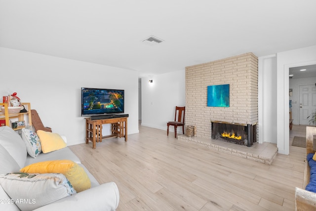 living room featuring visible vents, a brick fireplace, and wood finished floors