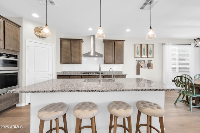 kitchen featuring stainless steel appliances, light stone countertops, decorative light fixtures, and wall chimney exhaust hood