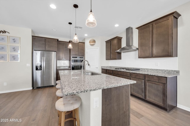 kitchen featuring sink, light stone counters, appliances with stainless steel finishes, pendant lighting, and wall chimney range hood