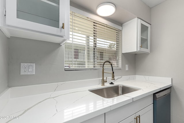 kitchen with a sink, dishwashing machine, glass insert cabinets, white cabinets, and light stone countertops