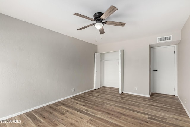 unfurnished bedroom with baseboards, a ceiling fan, visible vents, and wood finished floors