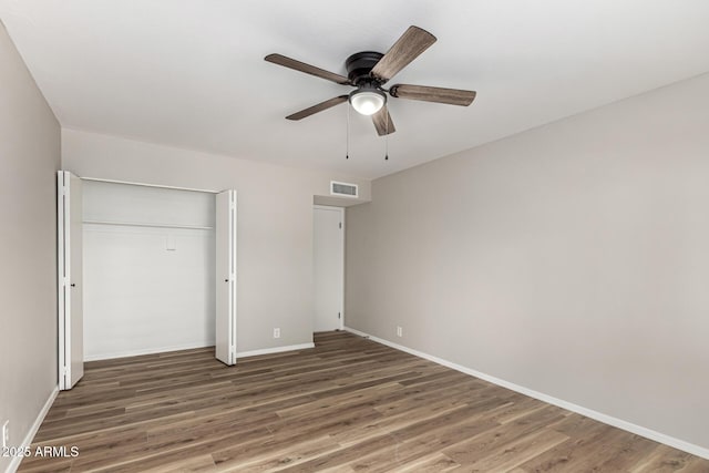 unfurnished bedroom featuring a ceiling fan, a closet, baseboards, visible vents, and wood finished floors