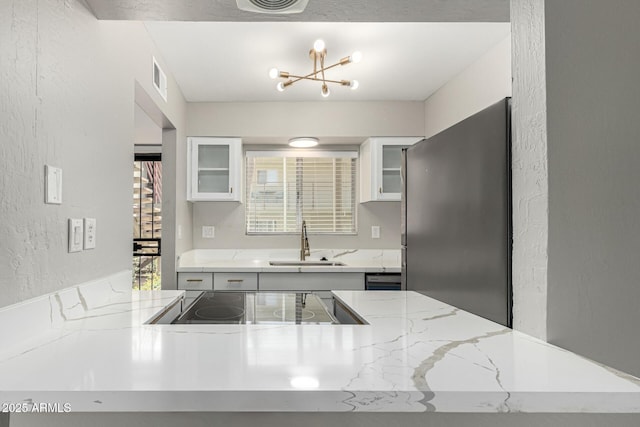 kitchen with a sink, freestanding refrigerator, visible vents, a chandelier, and cooktop