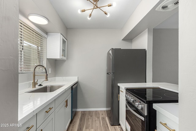 kitchen with a sink, light wood-style flooring, light stone countertops, a notable chandelier, and appliances with stainless steel finishes