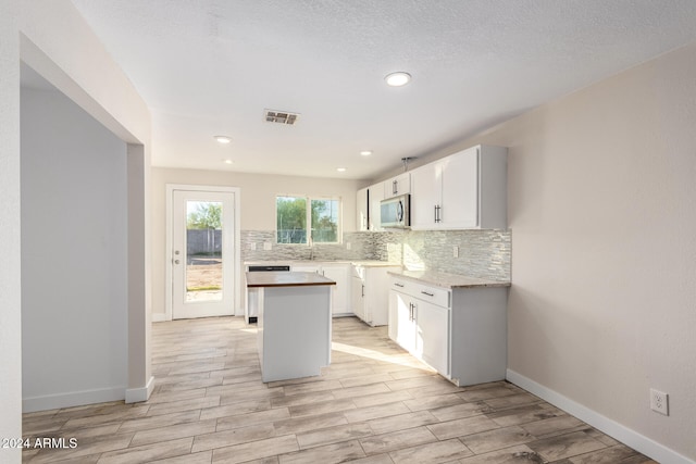 kitchen featuring light wood-type flooring, tasteful backsplash, a textured ceiling, white cabinets, and a center island