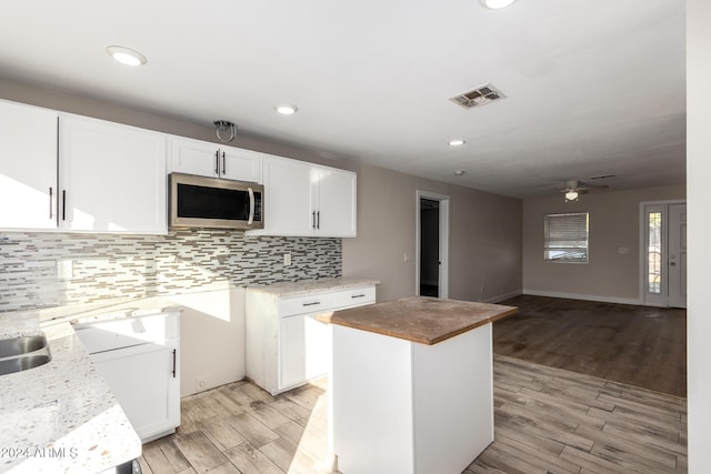 kitchen with a center island, white cabinets, ceiling fan, light wood-type flooring, and light stone counters