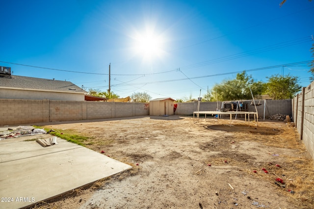 view of yard featuring a trampoline, a storage unit, and a patio area