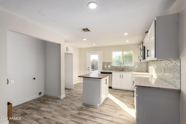 kitchen with sink, light hardwood / wood-style flooring, butcher block countertops, a kitchen island, and white cabinetry