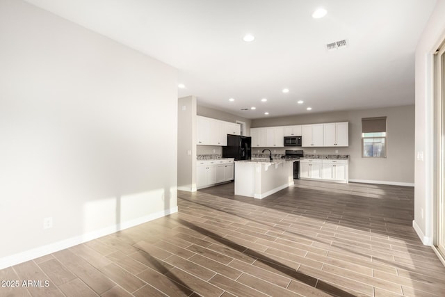 kitchen featuring a sink, black appliances, visible vents, a kitchen bar, and baseboards