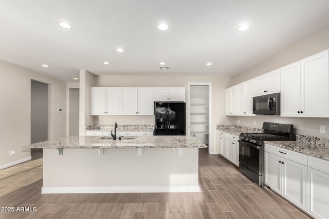 kitchen featuring light wood finished floors, a sink, a kitchen bar, white cabinetry, and black appliances