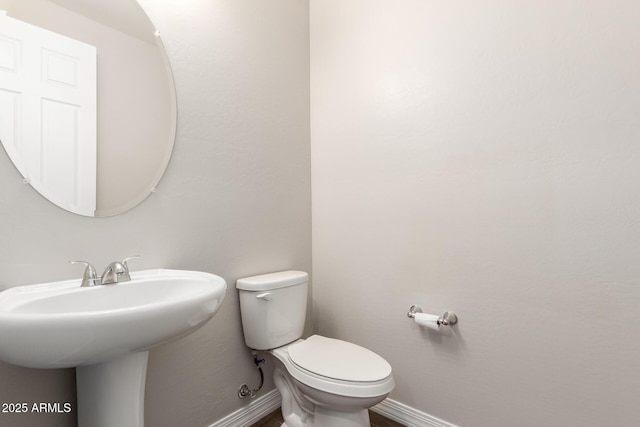 half bath with toilet, baseboards, and a sink