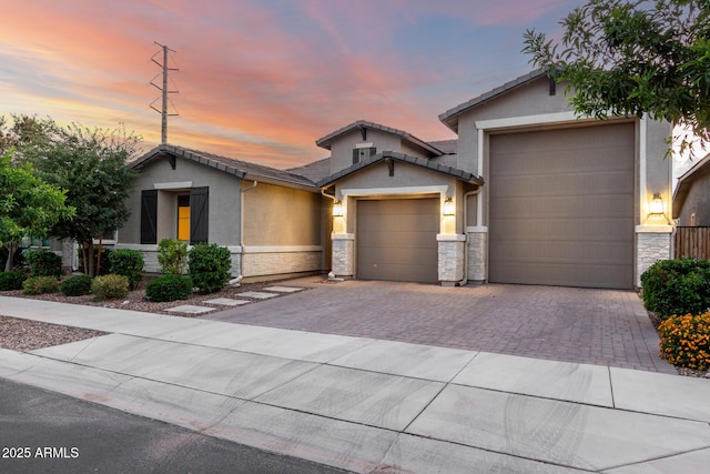 view of front of house featuring an attached garage, stone siding, stucco siding, a tile roof, and driveway