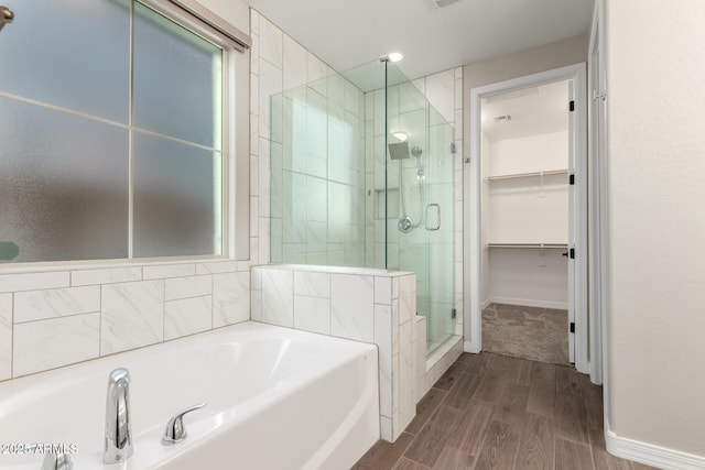 full bath featuring wood finished floors, baseboards, a stall shower, a walk in closet, and a garden tub