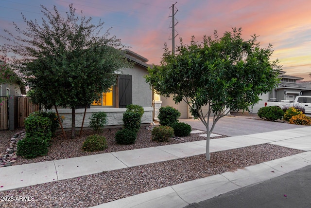 view of property hidden behind natural elements featuring concrete driveway, stucco siding, and fence
