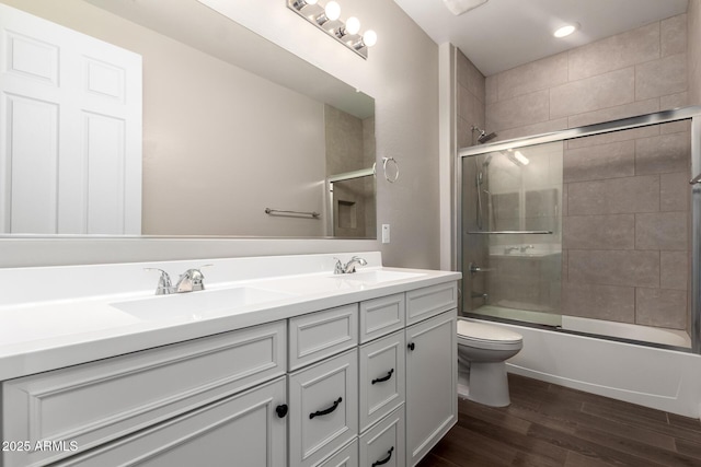 full bathroom featuring double vanity, toilet, wood finished floors, combined bath / shower with glass door, and a sink