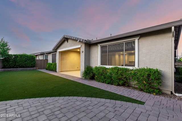 view of home's exterior featuring an attached garage, stucco siding, fence, and a lawn