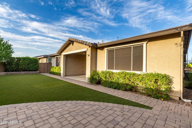 rear view of property featuring stucco siding, fence, a lawn, and a patio