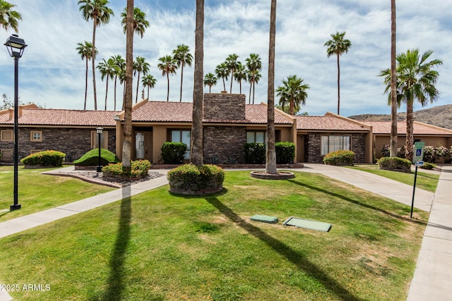 view of front facade with a front yard, stucco siding, a tile roof, and stone siding