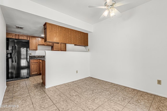 kitchen with visible vents, brown cabinetry, dark countertops, ceiling fan, and black fridge