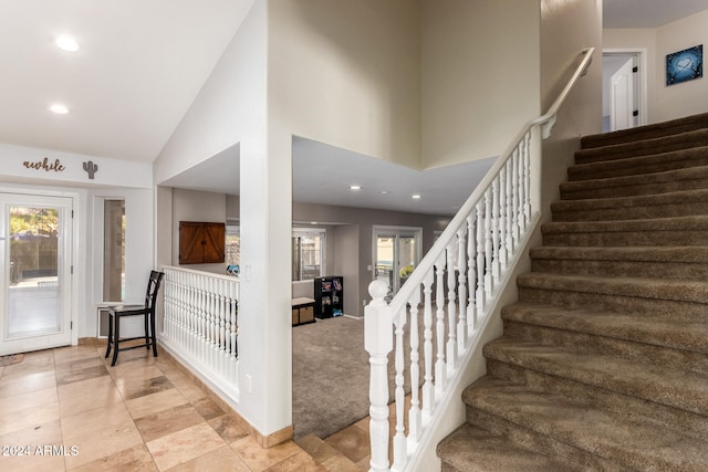 staircase with carpet flooring and high vaulted ceiling