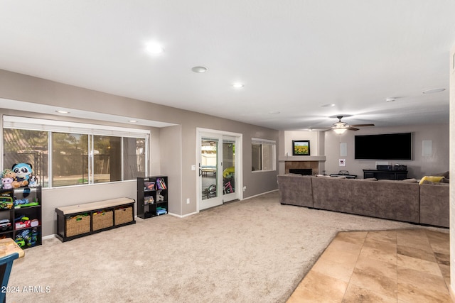 living room with a tile fireplace, light colored carpet, and ceiling fan