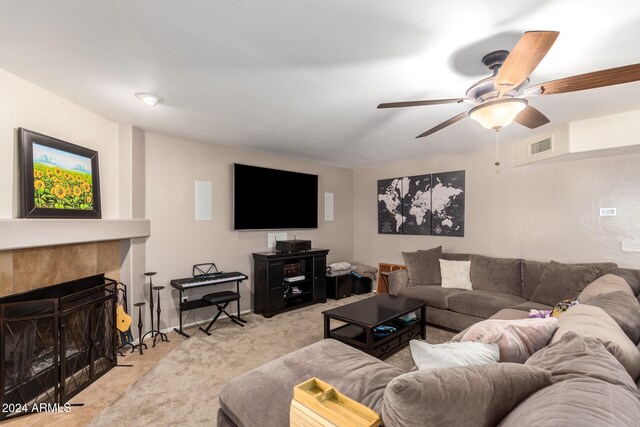 living room with a tiled fireplace, light colored carpet, and ceiling fan