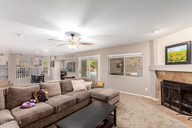 carpeted living room featuring a textured ceiling, a tile fireplace, ceiling fan, and french doors