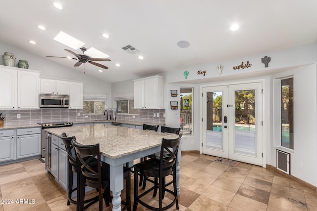 kitchen with white cabinets, appliances with stainless steel finishes, lofted ceiling with skylight, and light stone countertops