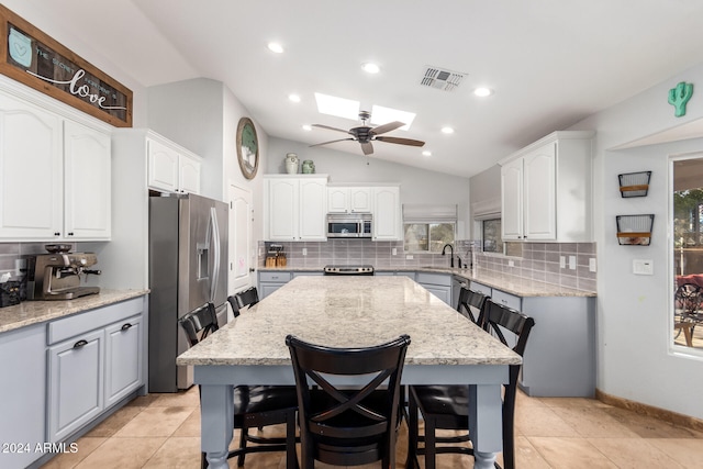 kitchen featuring white cabinetry, stainless steel appliances, lofted ceiling with skylight, and a breakfast bar