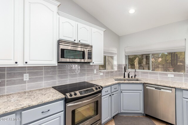 kitchen featuring stainless steel appliances, backsplash, sink, white cabinets, and lofted ceiling