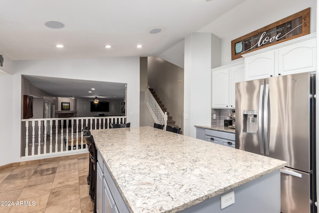 kitchen with stainless steel fridge, white cabinetry, a kitchen island, and vaulted ceiling