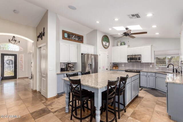 kitchen with a center island, white cabinets, sink, a skylight, and appliances with stainless steel finishes