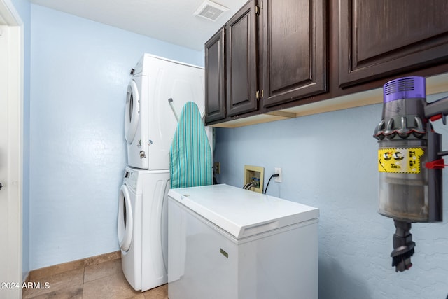 washroom featuring stacked washing maching and dryer, cabinets, and light tile patterned flooring