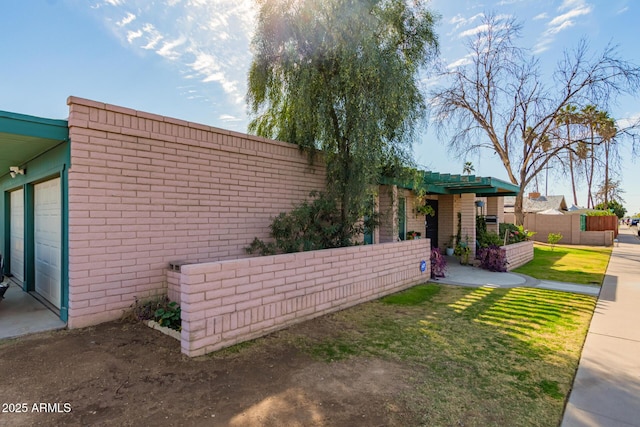 exterior space featuring an attached garage, a yard, fence, and brick siding