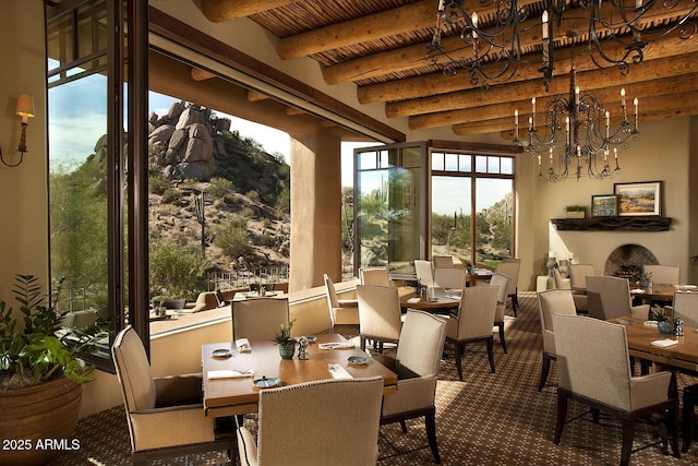 dining space featuring wooden ceiling, beamed ceiling, a fireplace, and a chandelier